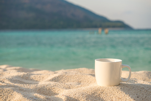 Coffee cup put on the tropical white sand island beach. Travel summer beach holiday, relaxation concept.