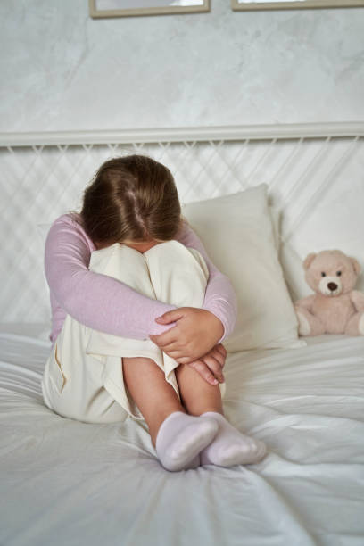 istock Elementary age girl sitting on bed with head hidden in legs 1618518742