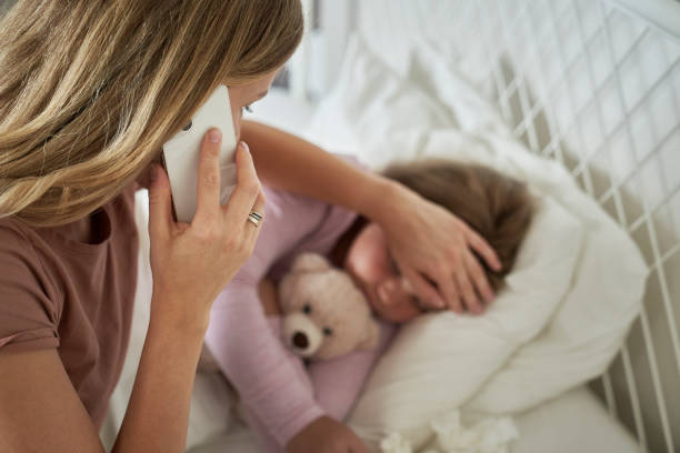 istock Mother calling a doctor while her daughter lying ill in bed 1618524642