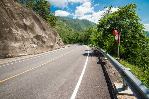 giro de carretera cuesta abajo con barrera de seguridad, espejo convexo y protección de muro de hormigón contra deslizamientos de tierra en las montañas. - thailand forest outdoors winding road fotografías e imágenes de stock