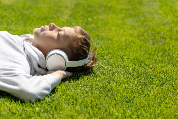 Um menino relaxando na grama, ouvindo música - foto de acervo