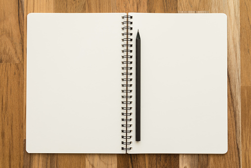 Flat lay of open blank spiral notepad or notebook and pencil on wooden table background. Office supply stationary, diary, organizer, business, education concept.