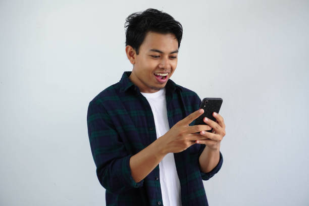 istock smiling young asian man looking to his mobile phone with happy expression isolated on white background 1618539694