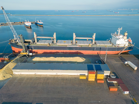 Aerial drone view above sea port. Cargo vessel is loading containers and bulk. Professional business logistics and transportation of cargo ship.