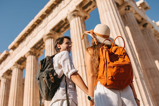 A rear view of a young couple standing in front of the Parthenon temple at Acropolis in Athens