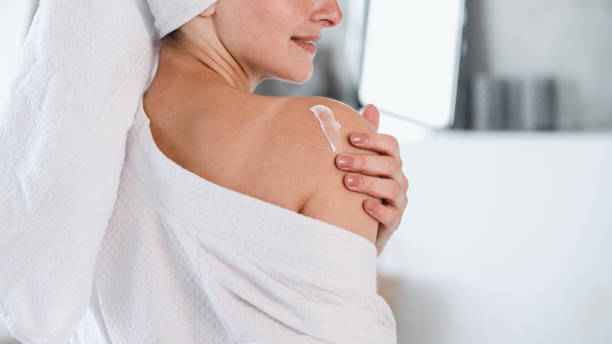 istock Woman in bathrobe applying moisturizer cream on shoulder 1618583466
