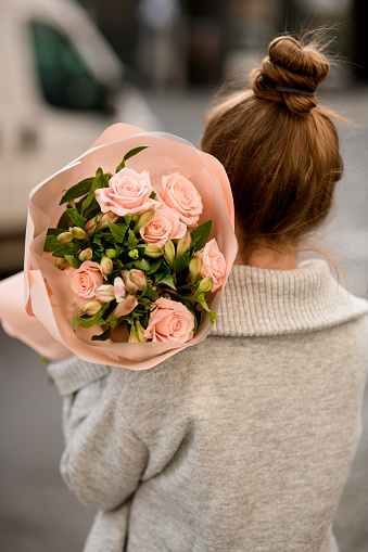 rear view of young attractive woman with beautiful bouquet of pink roses in wrapping paper in the hand