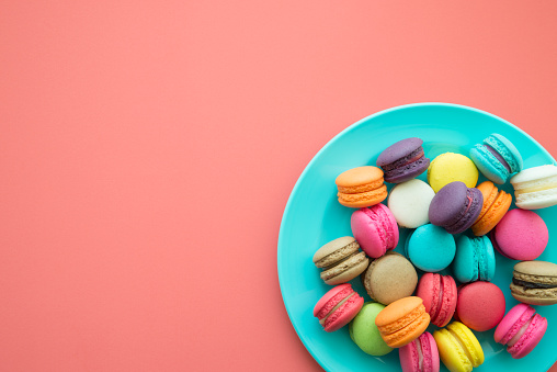 Colorful French macaroons in blue plate on pink background copy space. Dessert food, design concept.