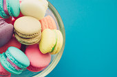 Colorful French macaroons in glass bowl on blue background copy space.