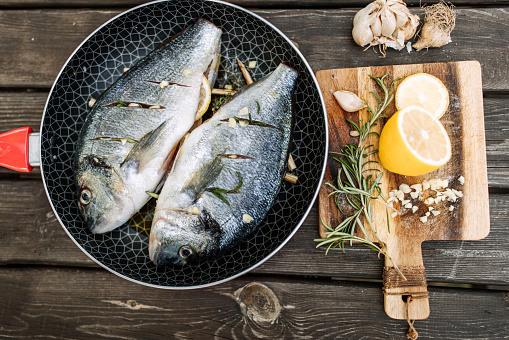 Dorada with the addition of spices, herbs and lemon on the grill pan located on a wooden background, top view
