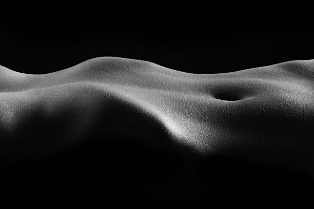Dimly lit close-up of a human torso laying horizontally Black and white bodyscape of woman's torso. human leg photos stock pictures, royalty-free photos & images