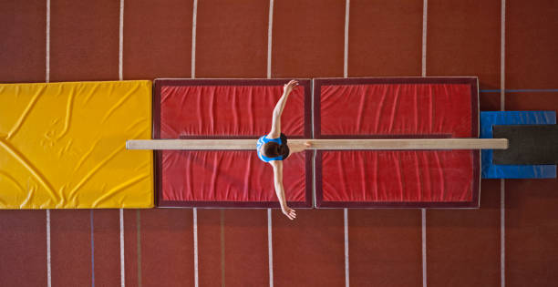 Overhead view of female gymnast performing on balance beam during practice in sports hall.