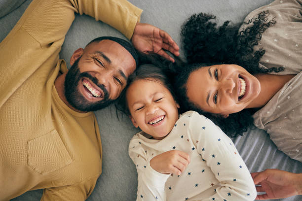 famiglia felice, sopra e sorriso bambino o felice con i genitori insieme al mattino ridendo in una camera da letto su un letto. rilassati, mamma e papà godono di tempo di qualità con il bambino con felicità, legame e amore - 4 of a kind foto e immagini stock