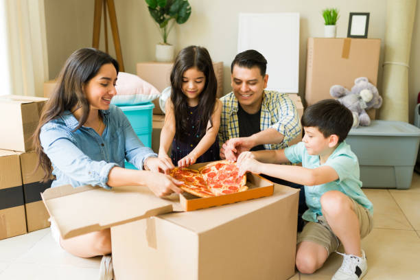 istock Cheerful family taking a break and eating pizza together after unpacking boxes while moving into a new house or apartment 1618680921