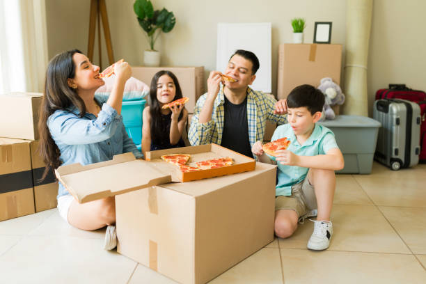 istock Relaxed family having dinner eating pizza on cardboard boxes while moving into a new house and unpacking 1618680952