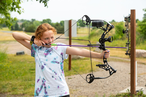 Close-up of a young girl practicing archery at an outdoor range on a summer day.