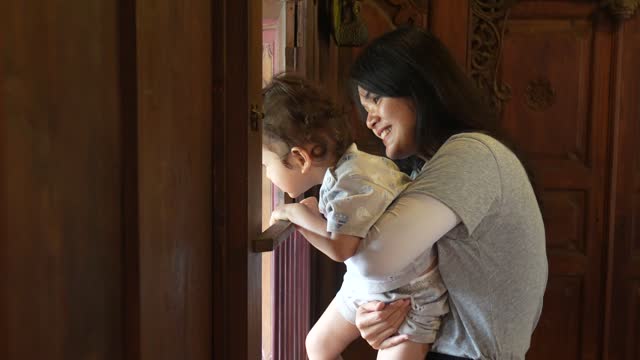 Beautiful asian  woman carrying her son opening window in joglo house