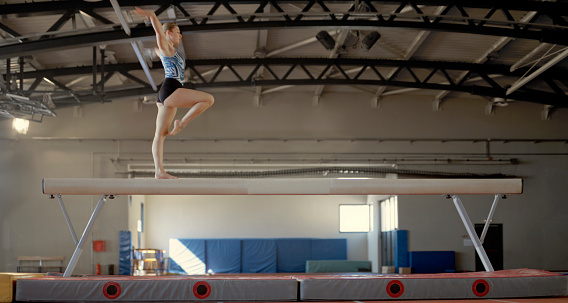 Female gymnast performing on balance beam during practice in sports hall.