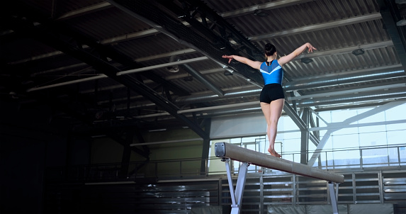Low angle view of female gymnast performing on balance beam during practice in sports hall.