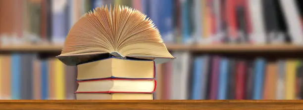 Image of an open book that lies on a stack of books against the background of bookshelves