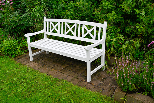 Wooden park bench painted white standing in green garden Sweden august 12 2023