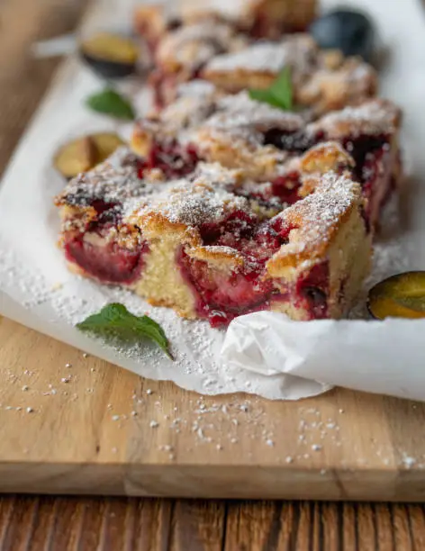 Traditional german cake with plums and crumbles. Served sliced and ready to eat on rustic and wooden cutting board. Closeup, front view with selective focus