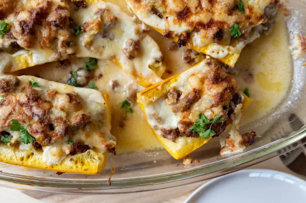 Delicious low carb meal with baked and stuffed squash. Filled with ground pork, herbs and cheese. Cooked with a bechamel sauce and served ready to eat on a table. Top view, closeup