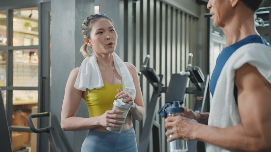 Multigeneration  of an Asian mid-adult woman and a 65-year senior man in sportswear friends talking when finishing strength training in the gym while having a protein shake and water