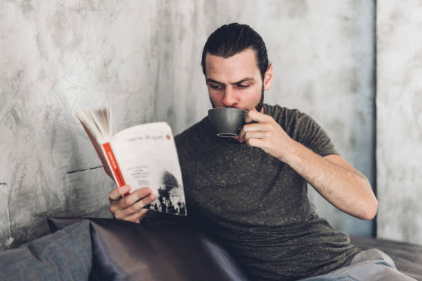 istock Handsome bearded hipster man relaxing holding and reading book with coffee while sitting on chair in cafe 1618768152
