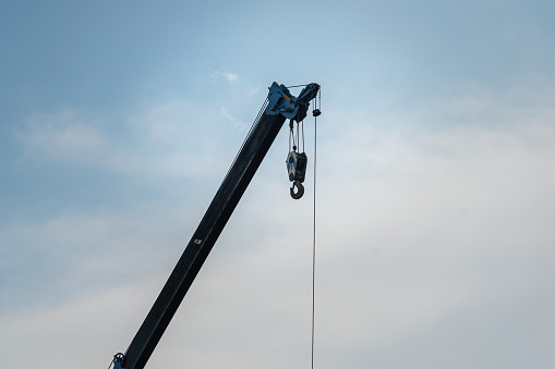 Construction building crane machine with hoisting chain block and hood during lifting the load object, on blue sky background. Industrial machine and equipment object.