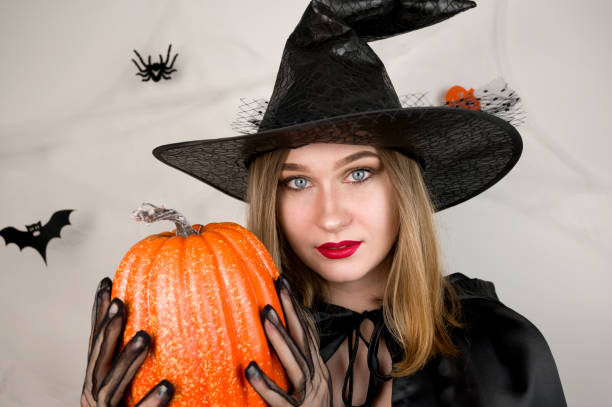 istock Halloween bannerwith female dresses as a witch holding pumkin on background with spiderweb 1618807077