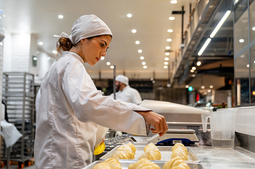 Woman working at a bakery making croissants and spreading them with sugar - baking concepts