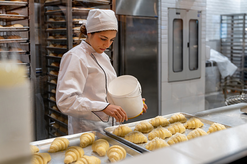 Happy Latin American female baker spreading coconut on some croissants while working at a pastry shop