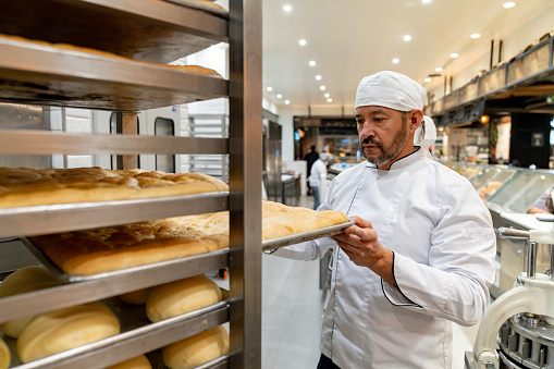 Latin American man working at a bakery moving a tray of freshly baked bread - baking concepts