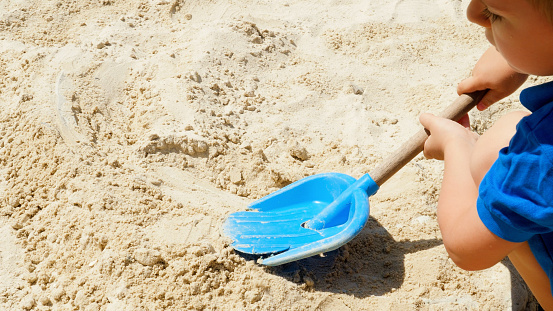 Closeup of little boy digging sand on the playground with plastic scoop or shovel.