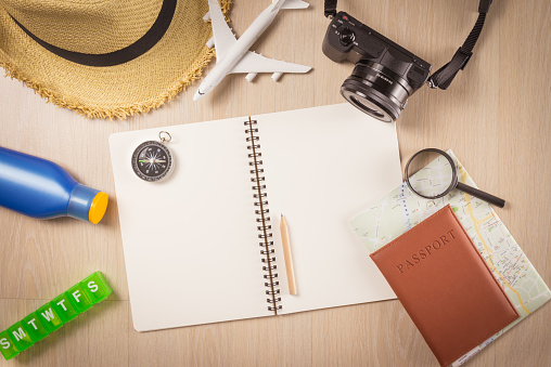Flat lay of personal necessary items, equipment for traveling with blank note pad on wooden background. Travel summer holiday, travel planning and preparation concept.