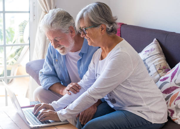 istock Smiling modern senior couple at home on sofa using laptop. Two elderly retirees enjoying free time and technological devices 1618876077