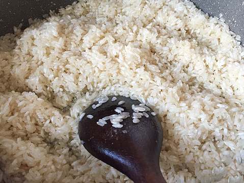 Cooking rice in a saucepan with wooden spoon, pilaf