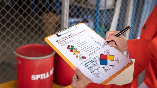 Action of safety officer is checking chemical hazard material form for correct the oil spill kit which is placed at front of chemical storage warehouse area in factory. Close-up and selective focus.