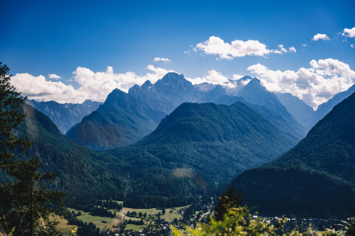 Scenic panoramic view of idyllic rolling hills landscape with blooming meadows and snowcapped alpine mountain peaks in the background on a beautiful sunny day with blue sky and clouds in summertime