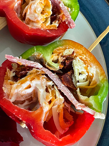 Stock photo showing elevated view of a healthy meal consisting of a red and green pepper sandwich consisting of capsicum filled with grated carrot and cheddar cheese, ham, crispy bacon and mayonnaise, held together by a wooden skewer and served on a blue rimmed plate.
