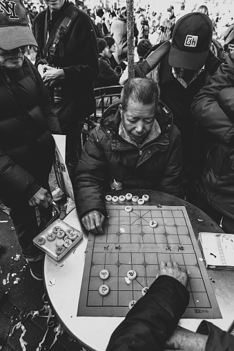 February 5, 2019: Chinese men playing Xiangqi (chinese chess) on the street in Chinatown in New York. Street black and white photo.