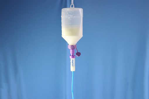 Enteral nutrition diet bottle hanging and infusing enteral diet throughout an infusion set. Blue background