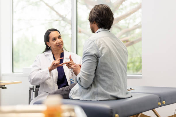 Female surgeon asks questions using American sign language to connect with the young adult male patient The female surgeon asks the young adult male patient questions using American sign language to connect with him. sign language stock pictures, royalty-free photos & images
