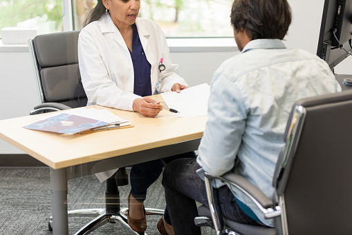 The female healthcare professional meets with the young adult male patient in her office to review a treatment plan she feels is the best option.