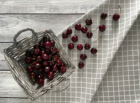 Red cherries fell out of a basket on a wooden table, top view.