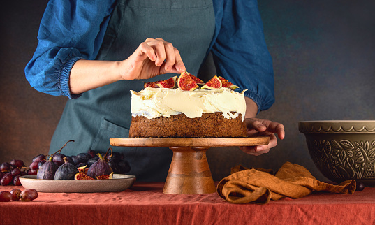 Woman is decorating fall pumpkin spice sponge cake with figs on buttercream topping