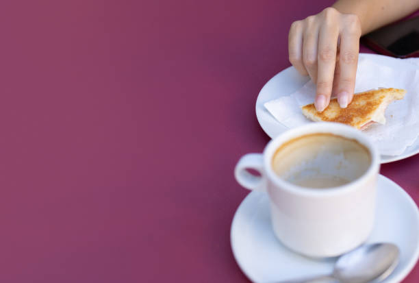 unrecognizable woman's hand holding a sandwich while having a snack with a cup of coffee. concept hotel business ,bar ,restaurant in the city.vertical image.