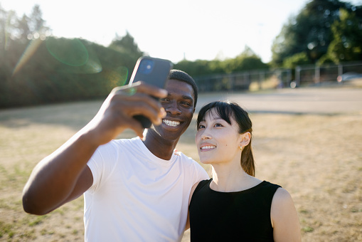 An African American man and Chinese American woman take a self portrait with a smart phone.  Shot in Seattle, Washington on a summer afternoon.
