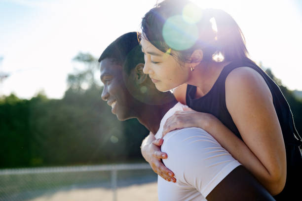 An African American man and Chinese American woman enjoy time together on a sunny summer day.  The woman rides on her boyfriends back.   Beautiful young love.